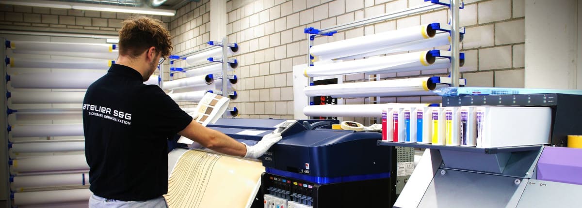 Werbetechniker in Digitaldruckerei an Maschine für Farbendruck.